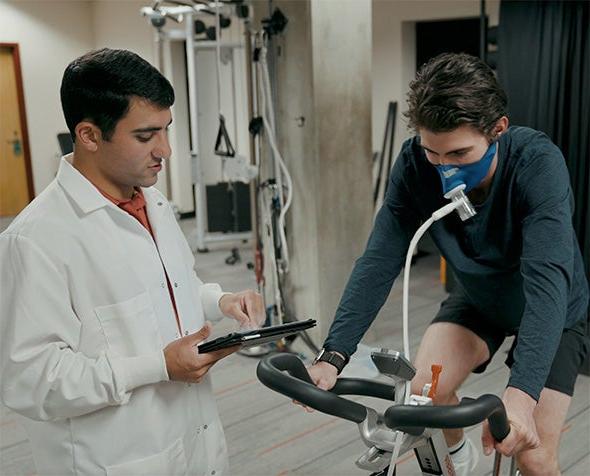 A student conducts physiology research with an athlete using a bicycle